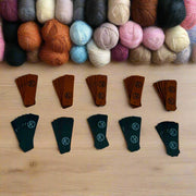 Top view of a craft table of colorful yarn balls and engraved leather tags.