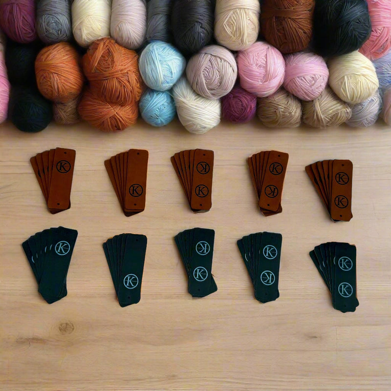 Top view of a craft table of colorful yarn balls and engraved leather tags.