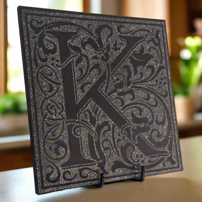 Black granite tile that is engraved around a floral design with the letter K and a solid border.